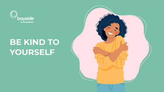 illustration showing a woman with dark curly hair and yellow sweater on a green background hugging herself with the text be kind to yourself and Bayside Psychotherapy logo