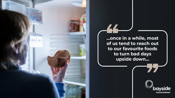 back of the person with short blonde hair and a blue sweater holding a cake in front of the open fridge on the left, and a meme style quotes about food with white fonts on a black background on the right, and the advice about how you can overcome emotional eating on a dusty pink background at the bottom right
