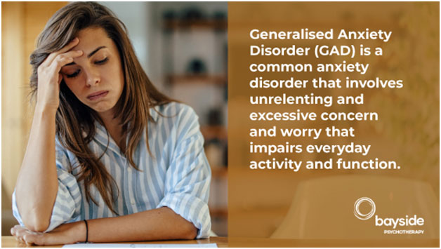 sad young woman with long brown hair wearing a striped shirt holding her head in her right hand on the left and the definition of the anxiety disorder on a brownish background on the right with the Bayside Psychotherapy logo