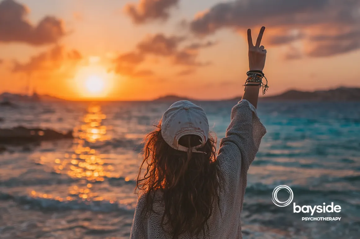 a girl standing in front of the ocean with peace sign