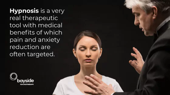 image of a white skin woman with a white t-shirt in a hypnosis state and a man with white hair talking to her with a text about hypnosis as a real therapeutic tool and with the Bayside Psychotherapy logo at the bottom left